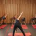 Yoga class with diverse adults stretching on mats in a cozy wooden studio.